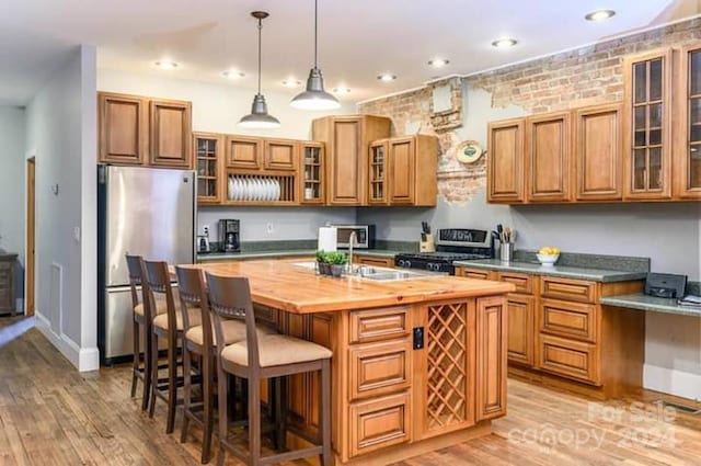 kitchen featuring appliances with stainless steel finishes, butcher block countertops, decorative light fixtures, light hardwood / wood-style flooring, and a kitchen island with sink