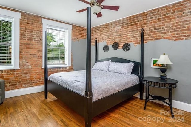 bedroom featuring brick wall, hardwood / wood-style floors, multiple windows, and ceiling fan