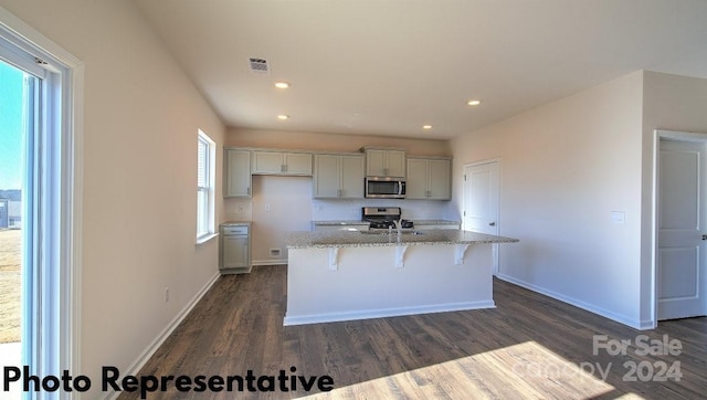 kitchen with a center island with sink, dark wood-type flooring, stainless steel appliances, and light stone countertops