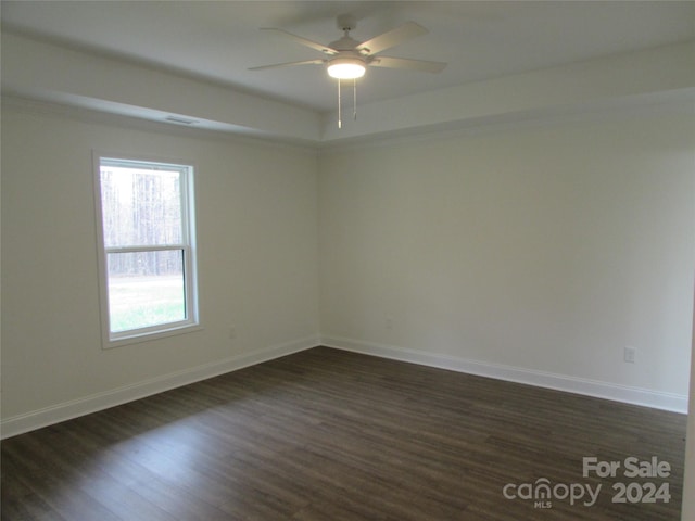 spare room with a raised ceiling, ceiling fan, and dark hardwood / wood-style flooring