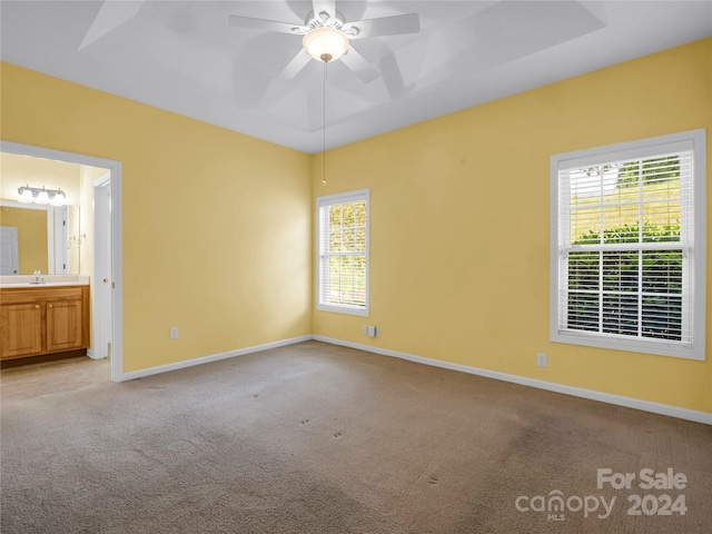 unfurnished bedroom featuring ceiling fan, multiple windows, ensuite bath, and light carpet