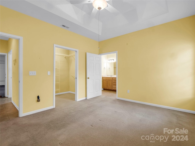 unfurnished bedroom with a spacious closet, a closet, ceiling fan, and light carpet