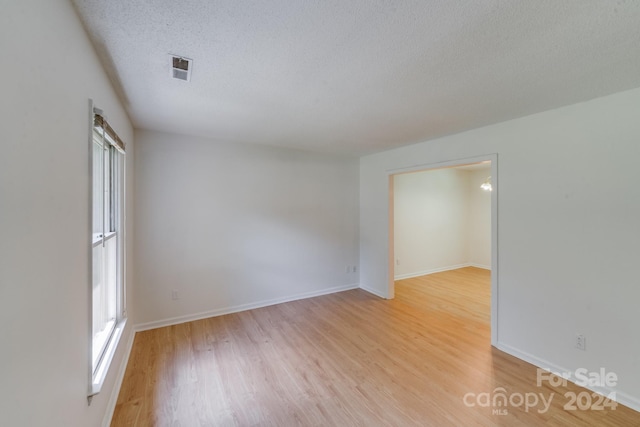 empty room with light wood-type flooring, visible vents, baseboards, and a textured ceiling