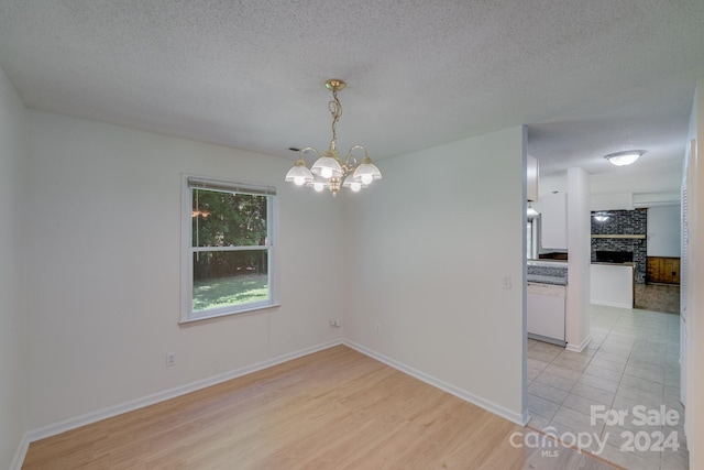 empty room with a notable chandelier, a brick fireplace, a textured ceiling, light wood-type flooring, and baseboards