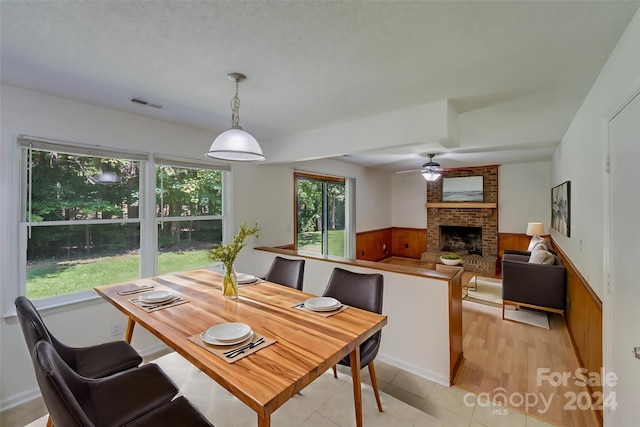 dining room featuring ceiling fan, light tile patterned floors, a wainscoted wall, visible vents, and a brick fireplace