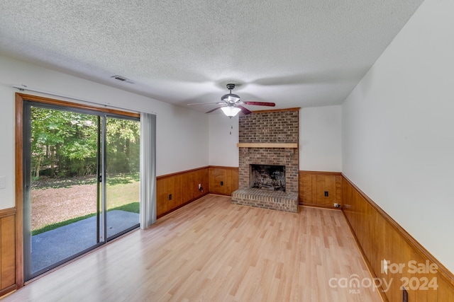 unfurnished living room featuring a brick fireplace, wainscoting, wooden walls, and a textured ceiling