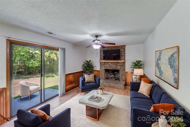 living area with a wainscoted wall, a textured ceiling, a brick fireplace, and light wood-style flooring