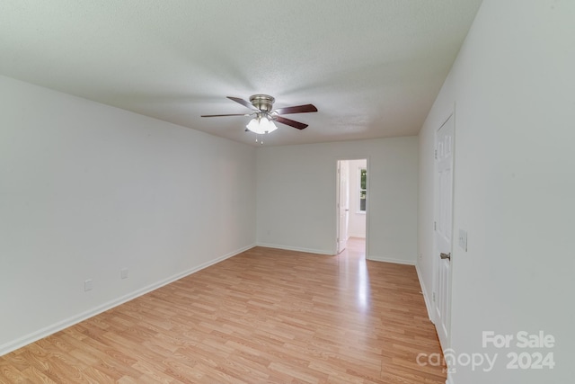 empty room with a textured ceiling, ceiling fan, baseboards, and light wood-style floors