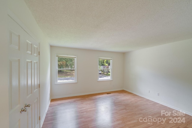 spare room with a textured ceiling, light wood finished floors, and baseboards