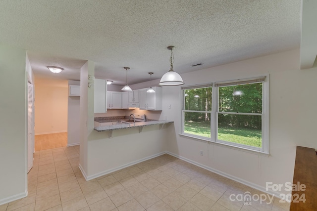 kitchen featuring light stone counters, a peninsula, visible vents, white cabinetry, and hanging light fixtures