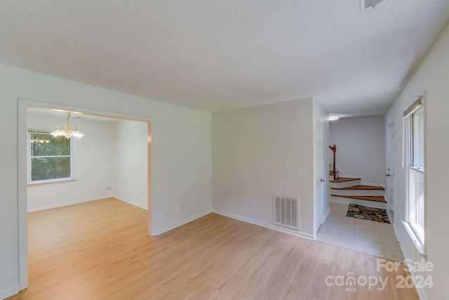 unfurnished room featuring visible vents, light wood-style flooring, stairs, a textured ceiling, and a chandelier