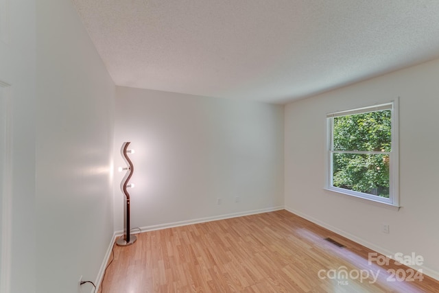 unfurnished room featuring light wood-style floors, visible vents, a textured ceiling, and baseboards