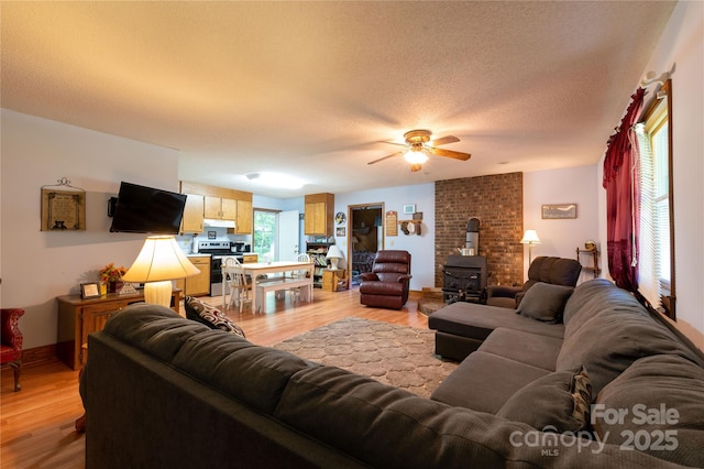 living room with ceiling fan, a wood stove, a textured ceiling, and light hardwood / wood-style flooring