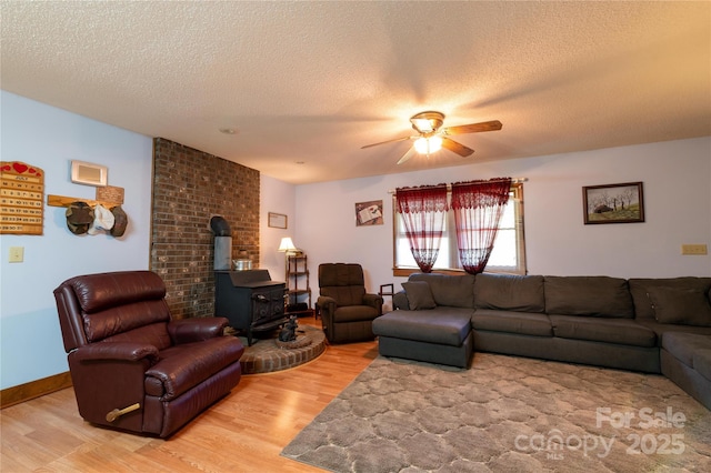 living room with a wood stove, ceiling fan, light hardwood / wood-style floors, and a textured ceiling