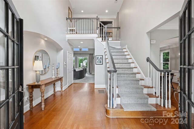 entryway with crown molding, visible vents, a towering ceiling, wood finished floors, and baseboards