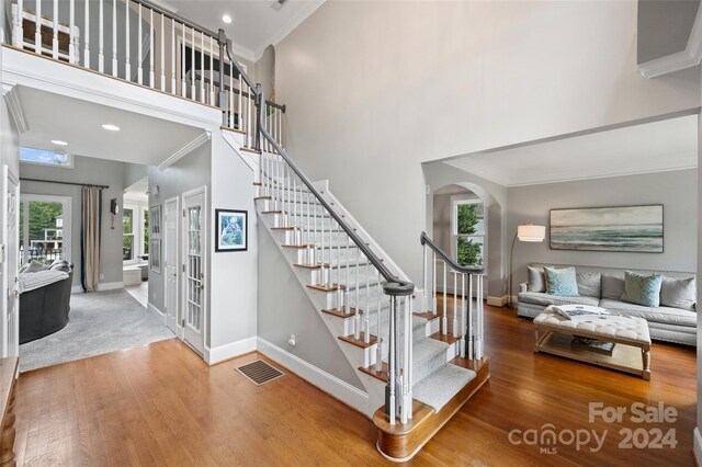 staircase with a towering ceiling, wood finished floors, visible vents, and crown molding