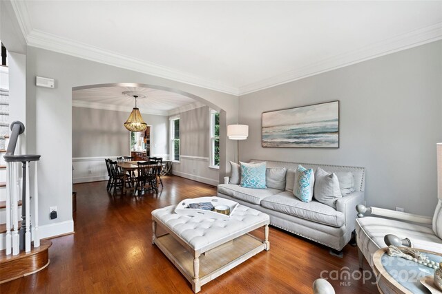 living area featuring arched walkways, baseboards, wood finished floors, and crown molding