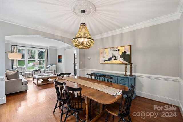 dining space with arched walkways, crown molding, wood finished floors, a chandelier, and baseboards