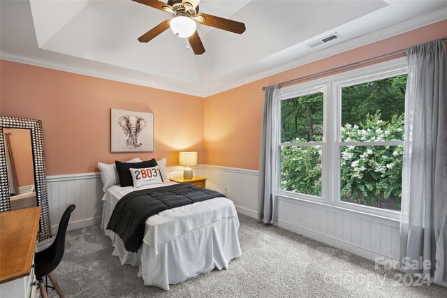 carpeted bedroom featuring visible vents, ornamental molding, a tray ceiling, and wainscoting