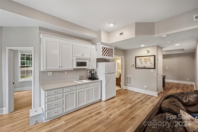 kitchen featuring white appliances, visible vents, white cabinets, light countertops, and a sink