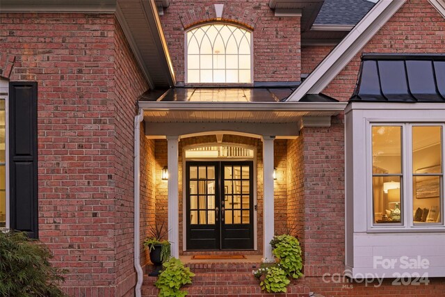 doorway to property featuring brick siding, a shingled roof, and french doors