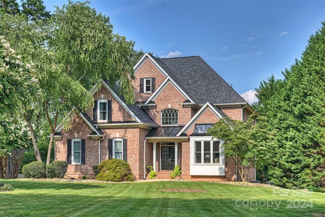 view of front facade with a front yard, brick siding, and roof with shingles