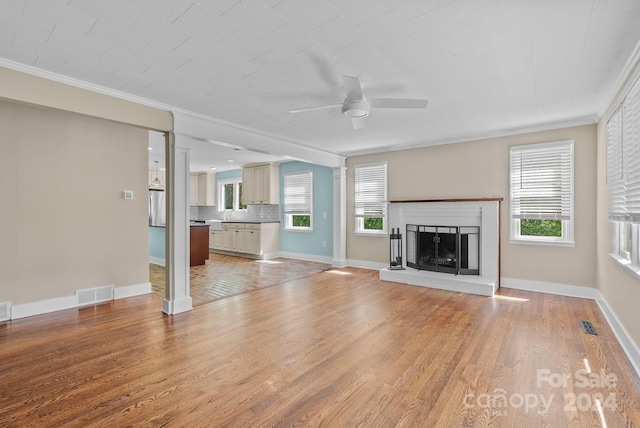 unfurnished living room featuring ceiling fan, hardwood / wood-style flooring, a brick fireplace, and ornamental molding