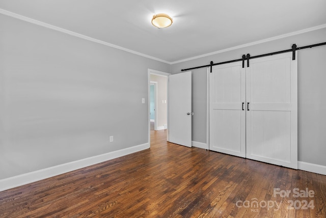 unfurnished bedroom with crown molding, a closet, a barn door, and dark hardwood / wood-style floors