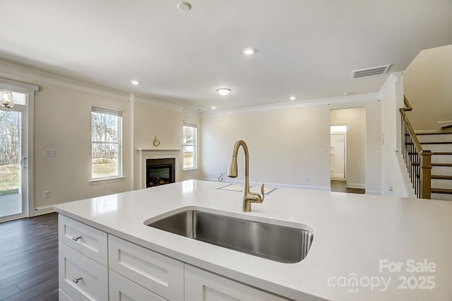 kitchen with light countertops, ornamental molding, open floor plan, white cabinetry, and a sink