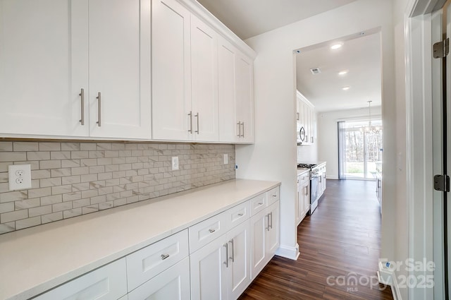 kitchen featuring dark wood-style floors, gas range oven, light countertops, backsplash, and white cabinetry