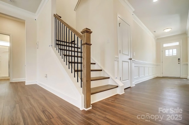 stairs featuring a decorative wall, ornamental molding, wainscoting, wood finished floors, and baseboards