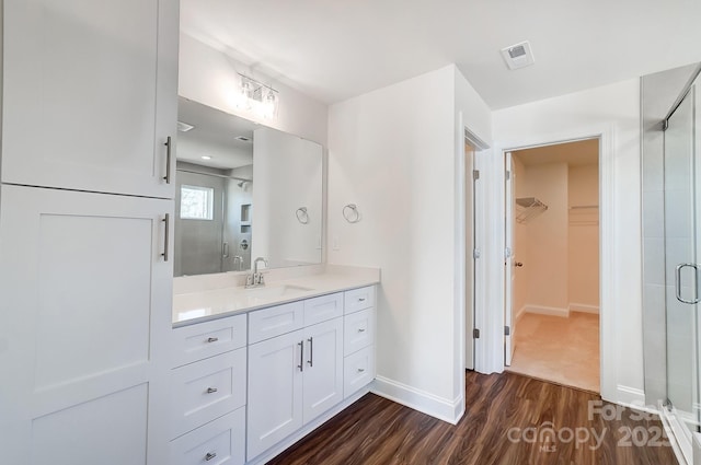 bathroom with a walk in closet, visible vents, a shower stall, vanity, and wood finished floors