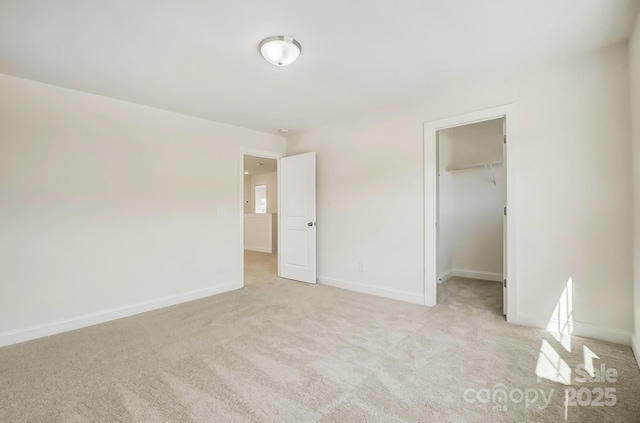 unfurnished bedroom featuring a closet, light colored carpet, a spacious closet, and baseboards