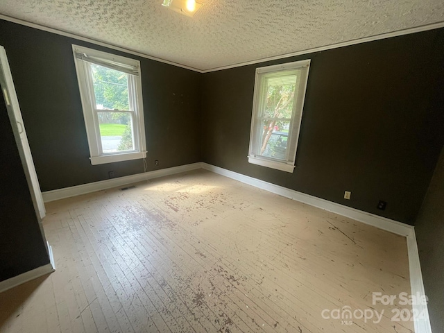 spare room featuring crown molding, a textured ceiling, and light hardwood / wood-style floors