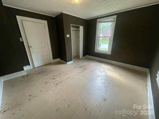 unfurnished bedroom featuring crown molding, light hardwood / wood-style floors, a closet, and a textured ceiling