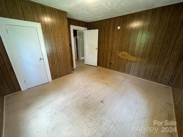 unfurnished bedroom with a textured ceiling, light hardwood / wood-style flooring, and wood walls