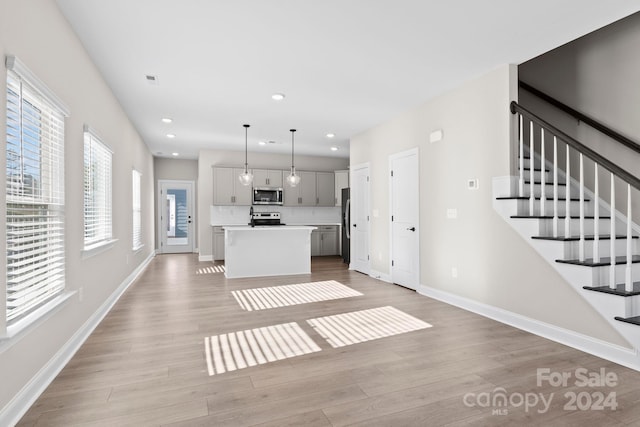 kitchen featuring hanging light fixtures, appliances with stainless steel finishes, gray cabinets, a kitchen island, and light wood-type flooring