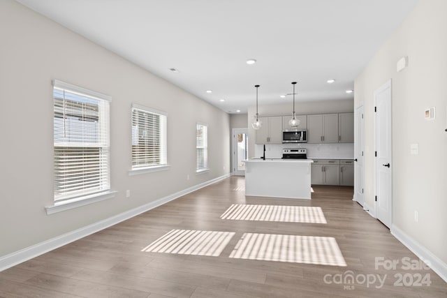 kitchen with light hardwood / wood-style floors, stainless steel appliances, gray cabinets, a kitchen island, and hanging light fixtures