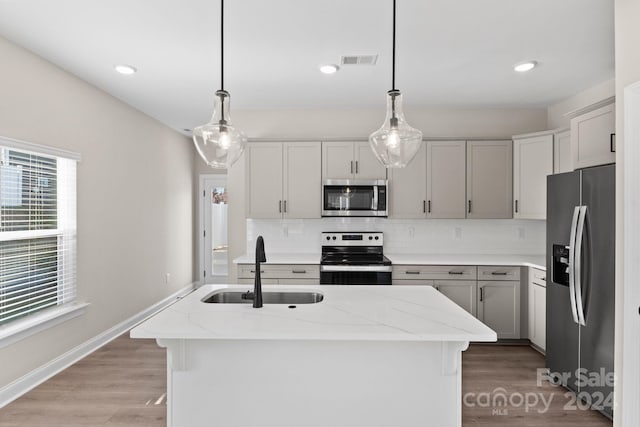 kitchen with a center island with sink, sink, light stone countertops, decorative light fixtures, and stainless steel appliances