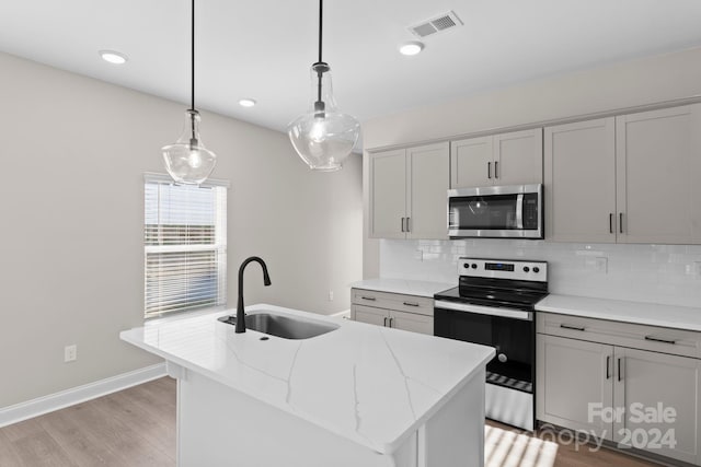 kitchen featuring a center island with sink, sink, light stone countertops, appliances with stainless steel finishes, and decorative light fixtures