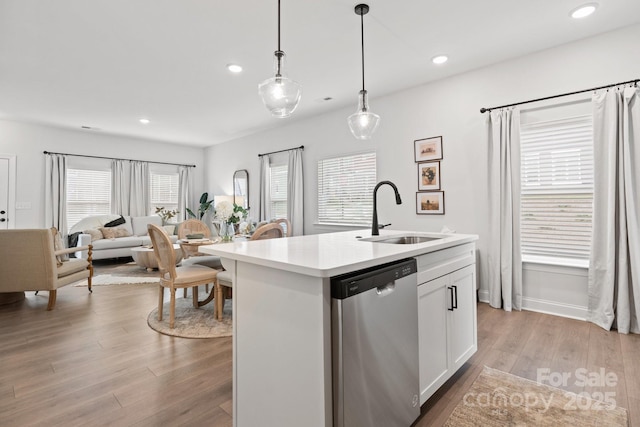 kitchen with sink, hanging light fixtures, stainless steel dishwasher, an island with sink, and white cabinets