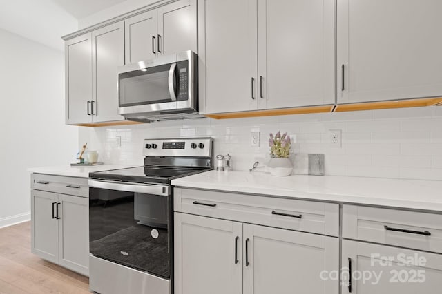 kitchen featuring stainless steel appliances, light stone countertops, light hardwood / wood-style flooring, and decorative backsplash