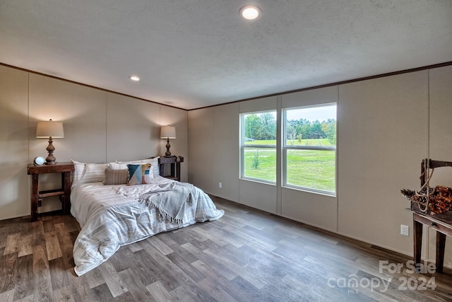 bedroom featuring wood-type flooring, a textured ceiling, and ornamental molding