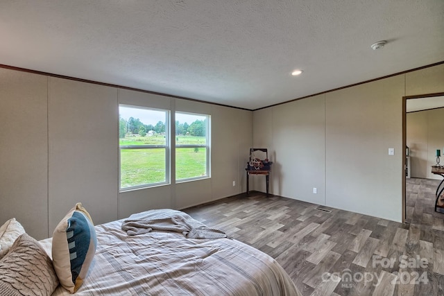 bedroom featuring wood-type flooring, a textured ceiling, and crown molding