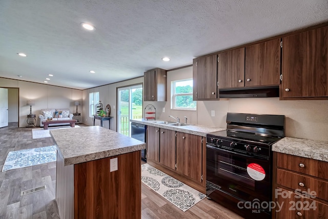 kitchen featuring black gas stove, dishwasher, a textured ceiling, a kitchen island, and light hardwood / wood-style flooring