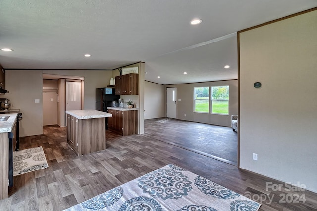 kitchen with vaulted ceiling, crown molding, a center island, hardwood / wood-style flooring, and black fridge