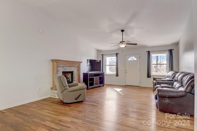 interior space featuring light wood-type flooring, vaulted ceiling, ceiling fan, and a brick fireplace