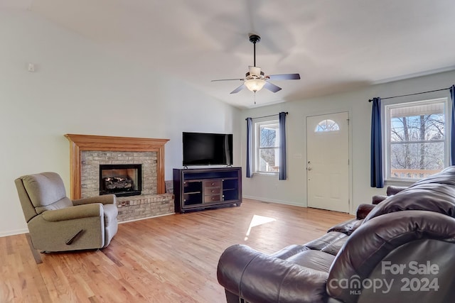 living room with ceiling fan, light wood-type flooring, a brick fireplace, and lofted ceiling