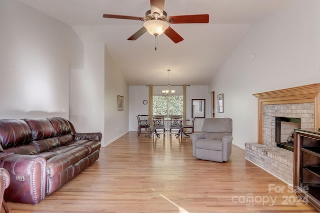 living room featuring light wood-type flooring, ceiling fan with notable chandelier, vaulted ceiling, and a fireplace