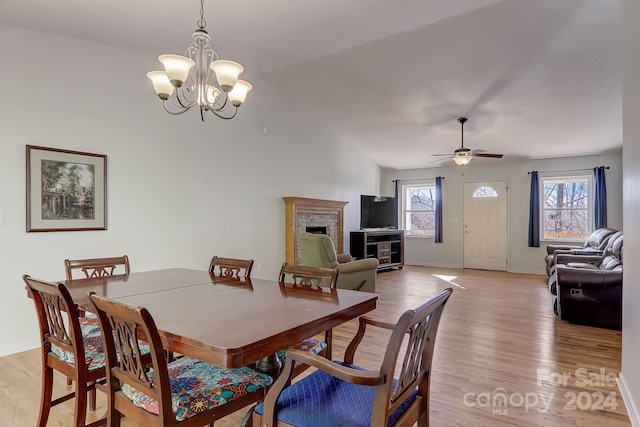 dining area featuring a fireplace, light hardwood / wood-style floors, and ceiling fan with notable chandelier